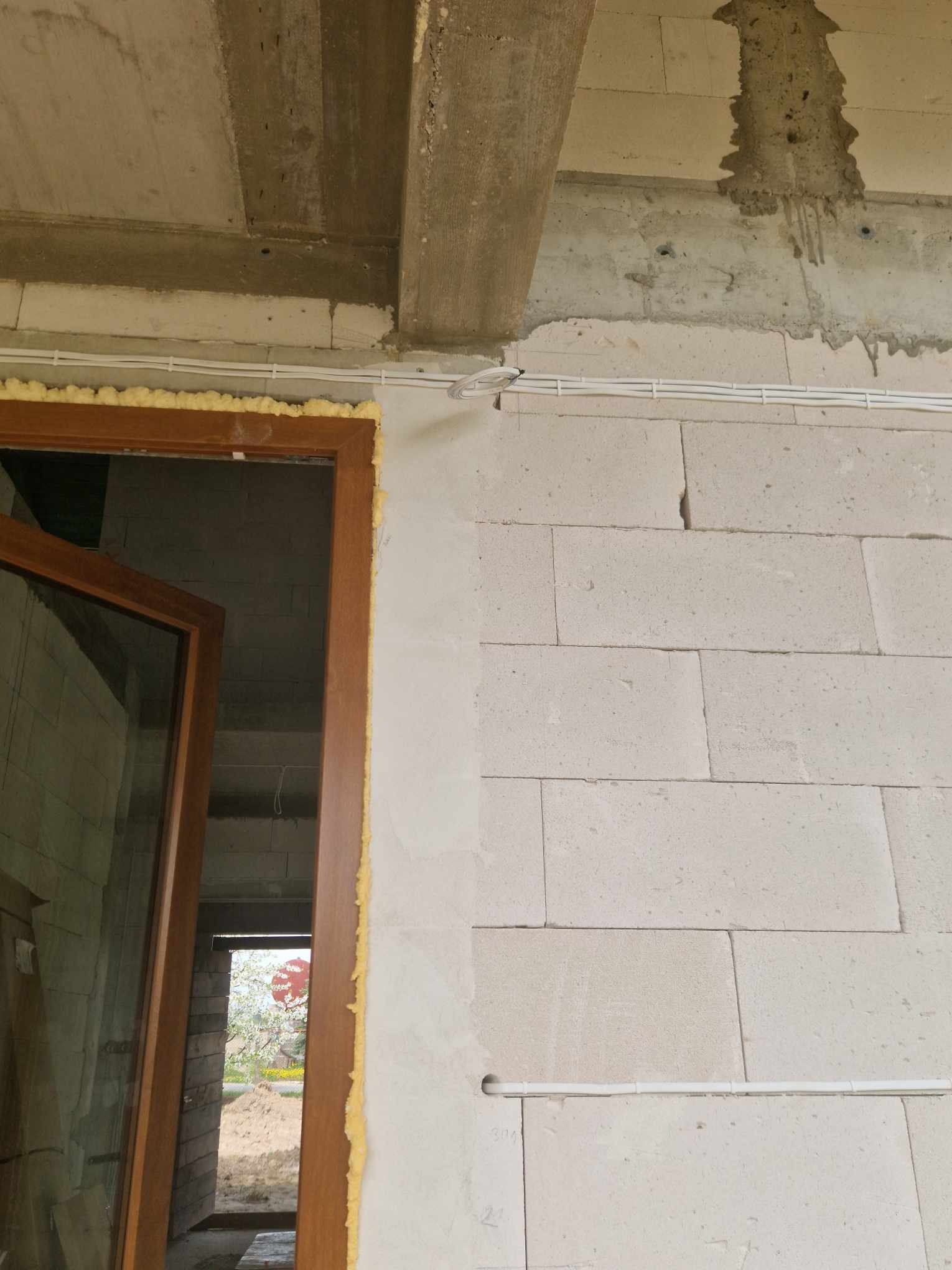 Surowy stan budynku: widoczne przewody elektryczne poprowadzone po ścianie z betonu komórkowego, osadzona stolarka okienna zabezpieczona pianką montażową, surowy betonowy strop.