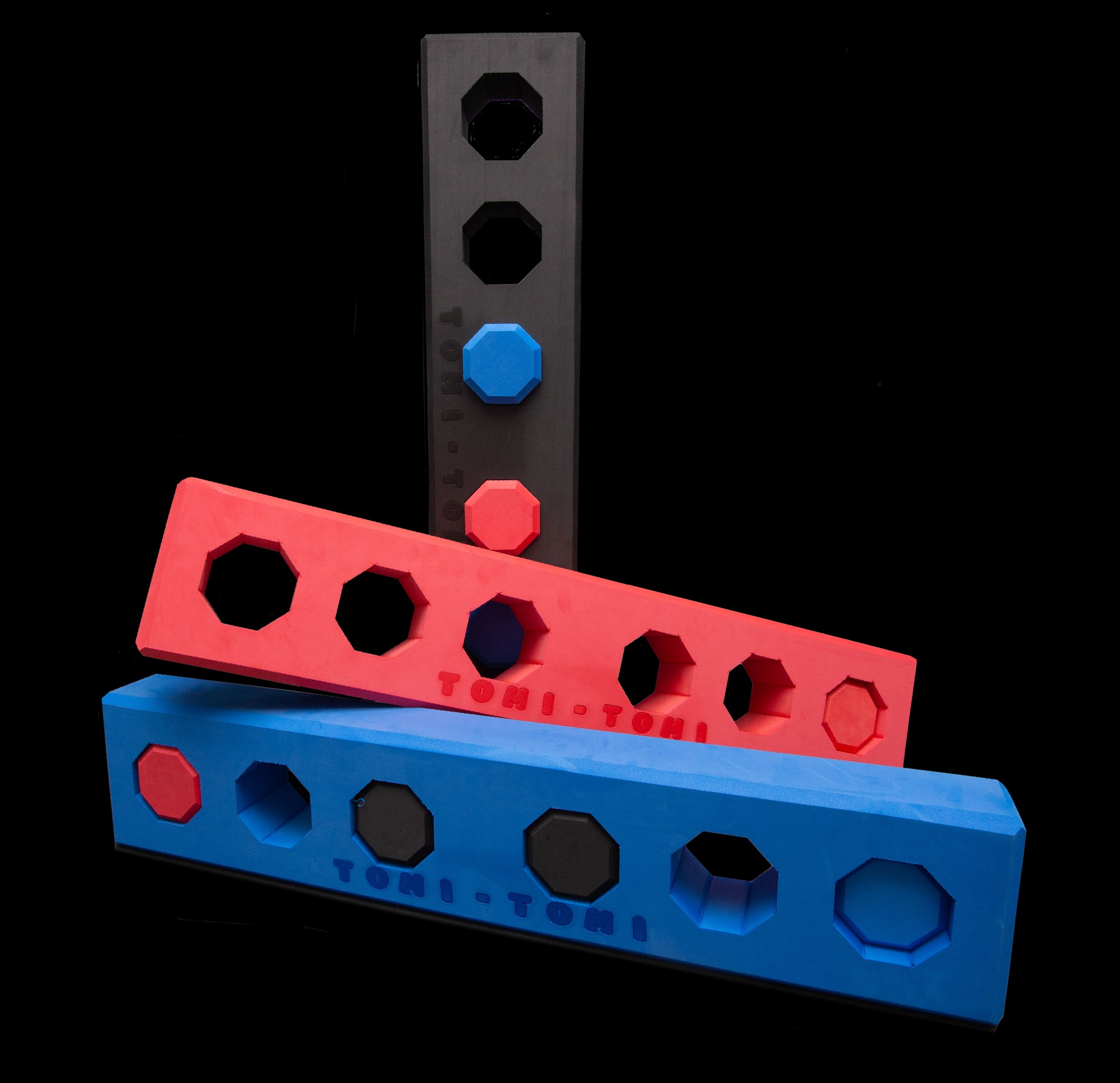 Trzy kolorowe, piankowe elementy z otworami w kształcie ośmiokątów, ułożone jeden na drugim, z napisem 'TONI-TONI' na dwóch z nich.