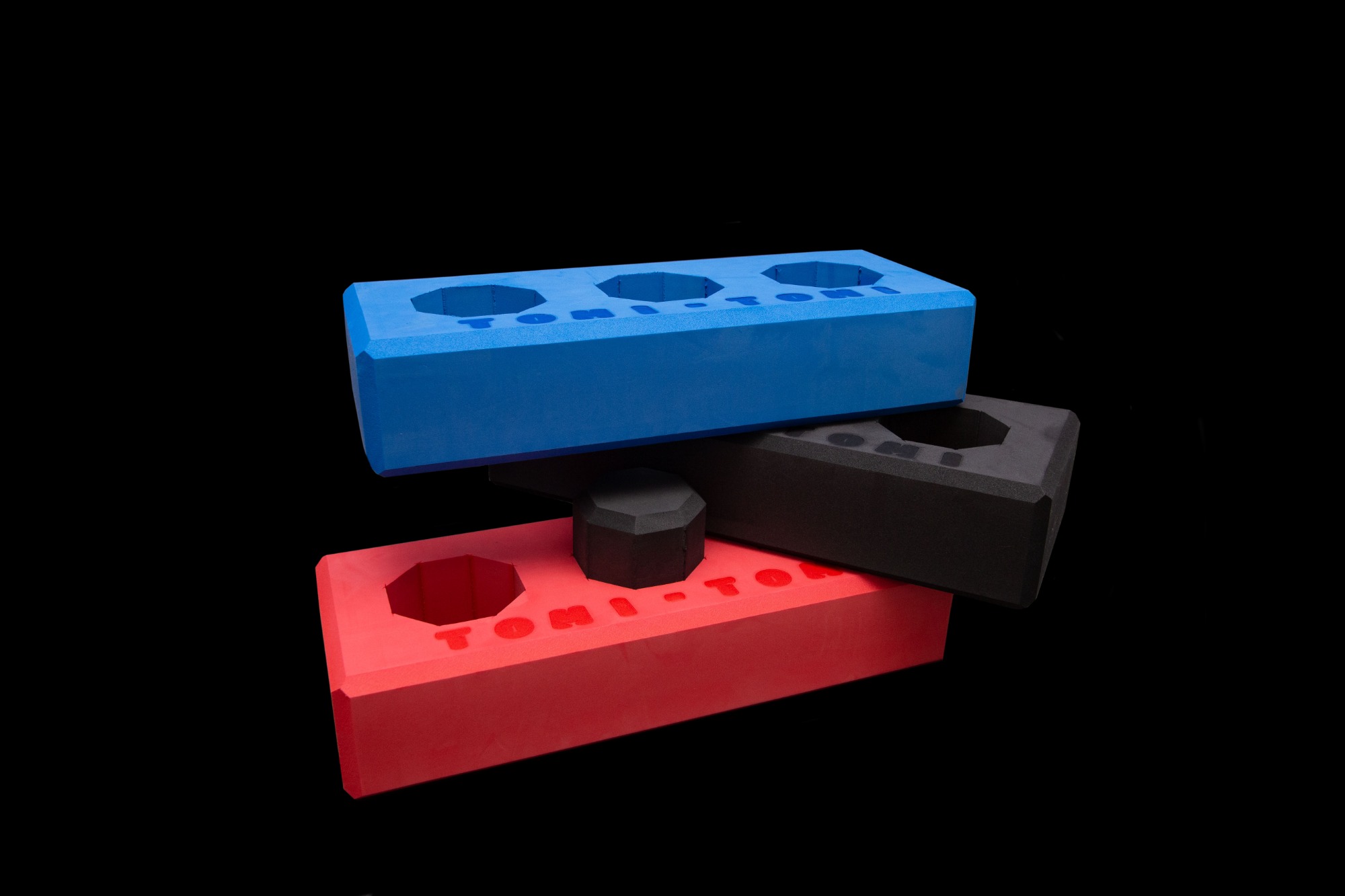 Kolorowe, piankowe klocki Tomi-Tomi ułożone w stos na czarnym tle, oferowane przez firmę z Łukowa. Klocki w kolorach niebieskim, czerwonym i czarnym.