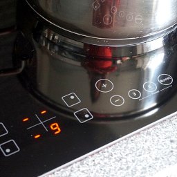 OLI - MAR Złota Rączka Robert Olędzki - Czarny garnek na płycie indukcyjnej ustawionej na moc 9, widoczne dotykowe panele sterowania i włączony tryb Boost.