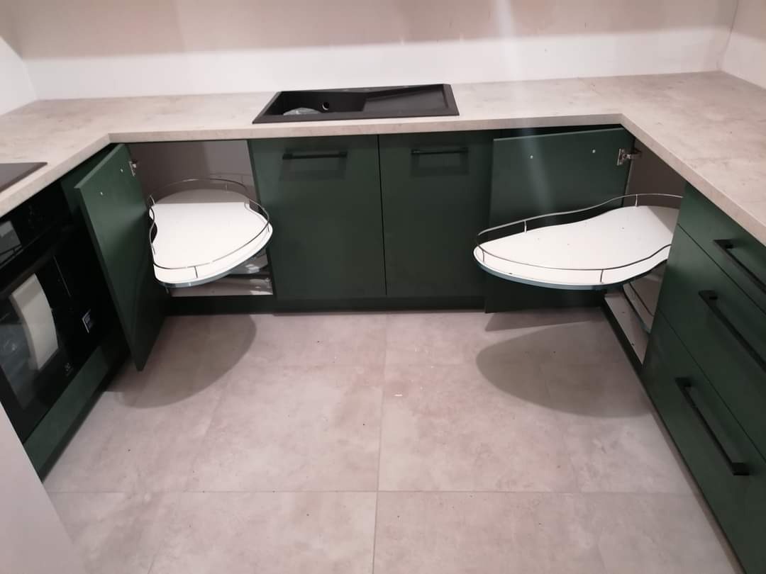 Nowoczesna kuchnia w odcieniach zieleni z zamontowanymi półkami obrotowymi w szafkach narożnych, widok z góry na wykończone wnętrze.