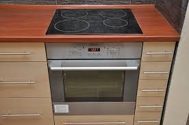 Wbudowana płyta indukcyjna i piekarnik elektryczny w jasnej zabudowie kuchennej z drewnianym blatem o ciepłej barwie.