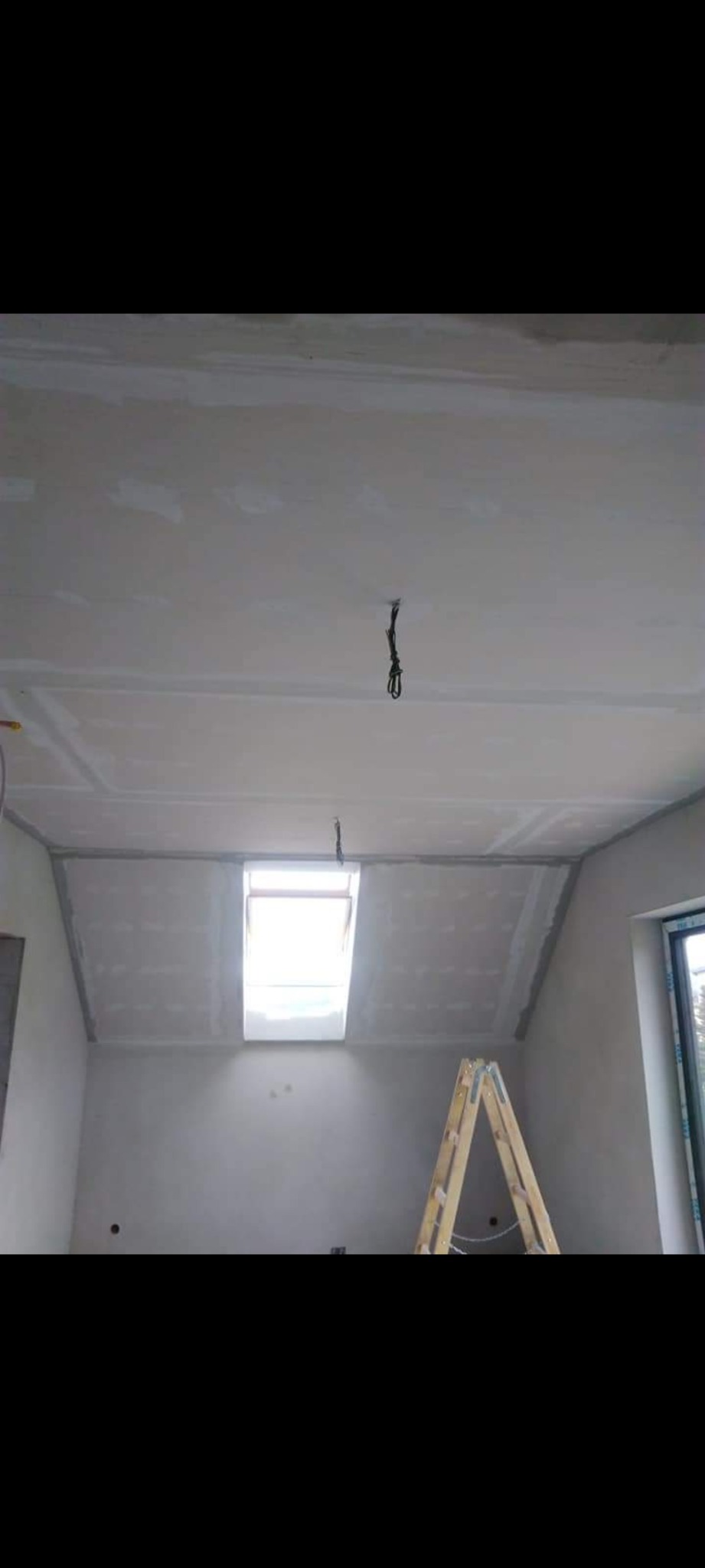 Poddasze po montażu płyt gipsowo-kartonowych, widoczne szpachlowane łączenia, okno dachowe i drabina rozstawiona w pomieszczeniu.