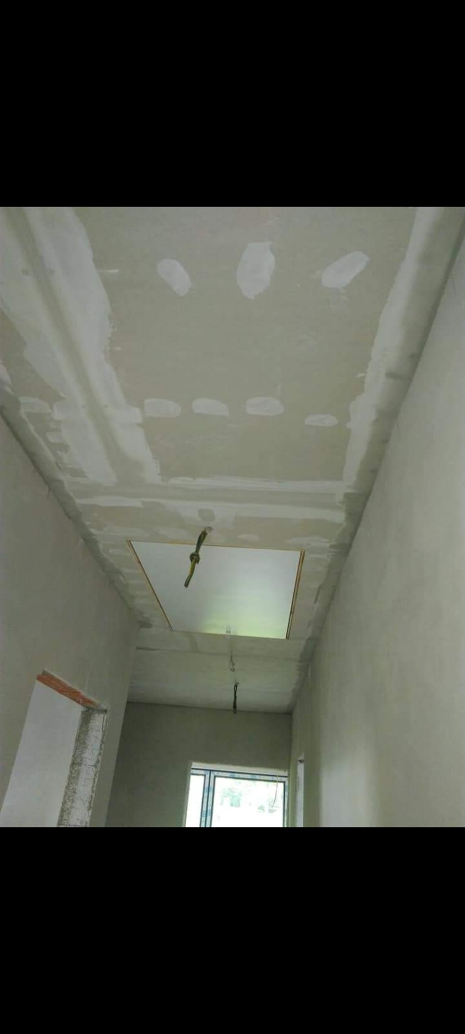 Sufit podwieszany z płyty karton gips, szpachlowany, z otworem rewizyjnym i wystającymi kablami, w korytarzu podczas remontu.