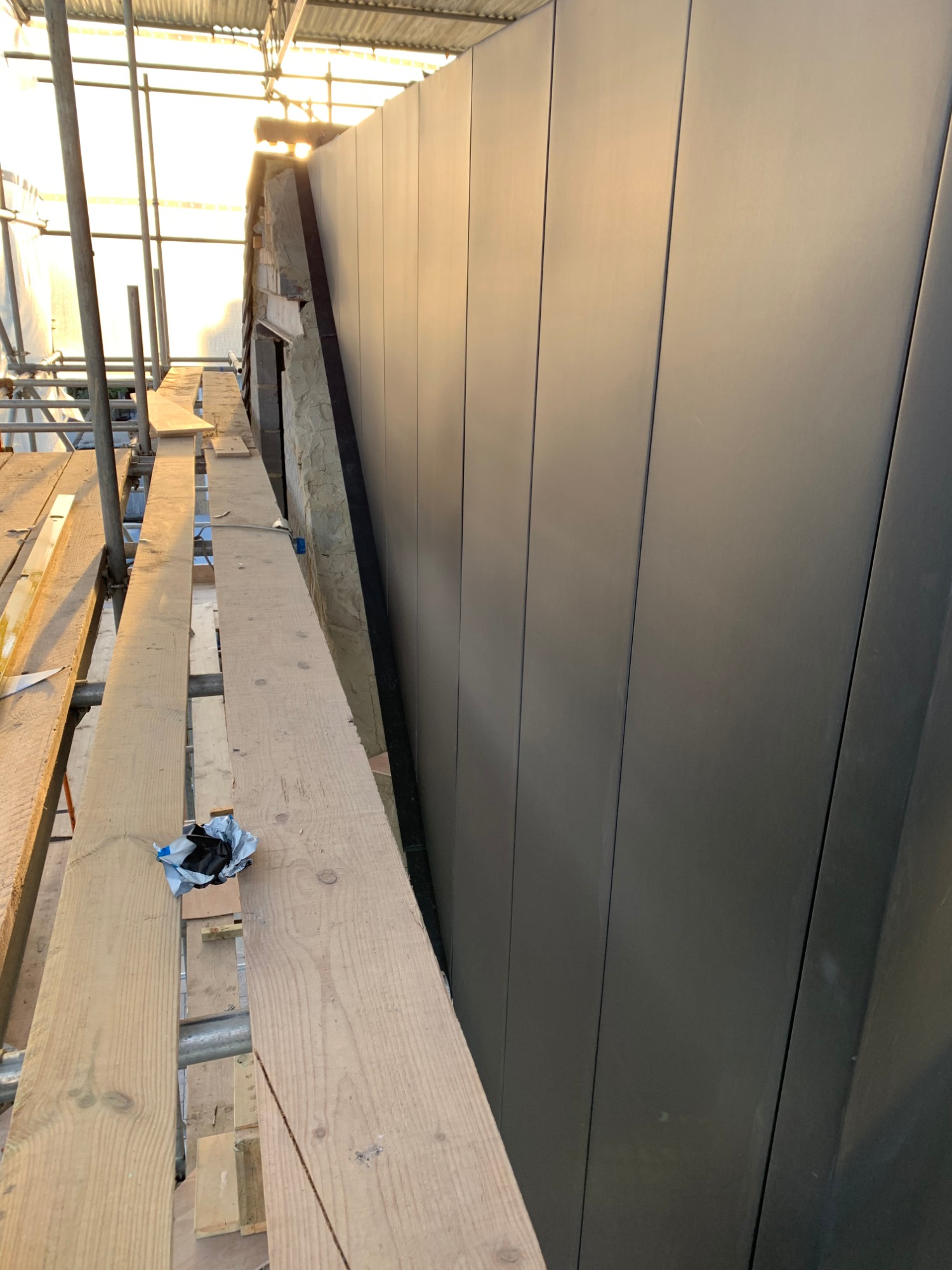 Montaż paneli elewacyjnych na rusztowaniu, widoczne ocieplenie budynku i elementy konstrukcyjne.