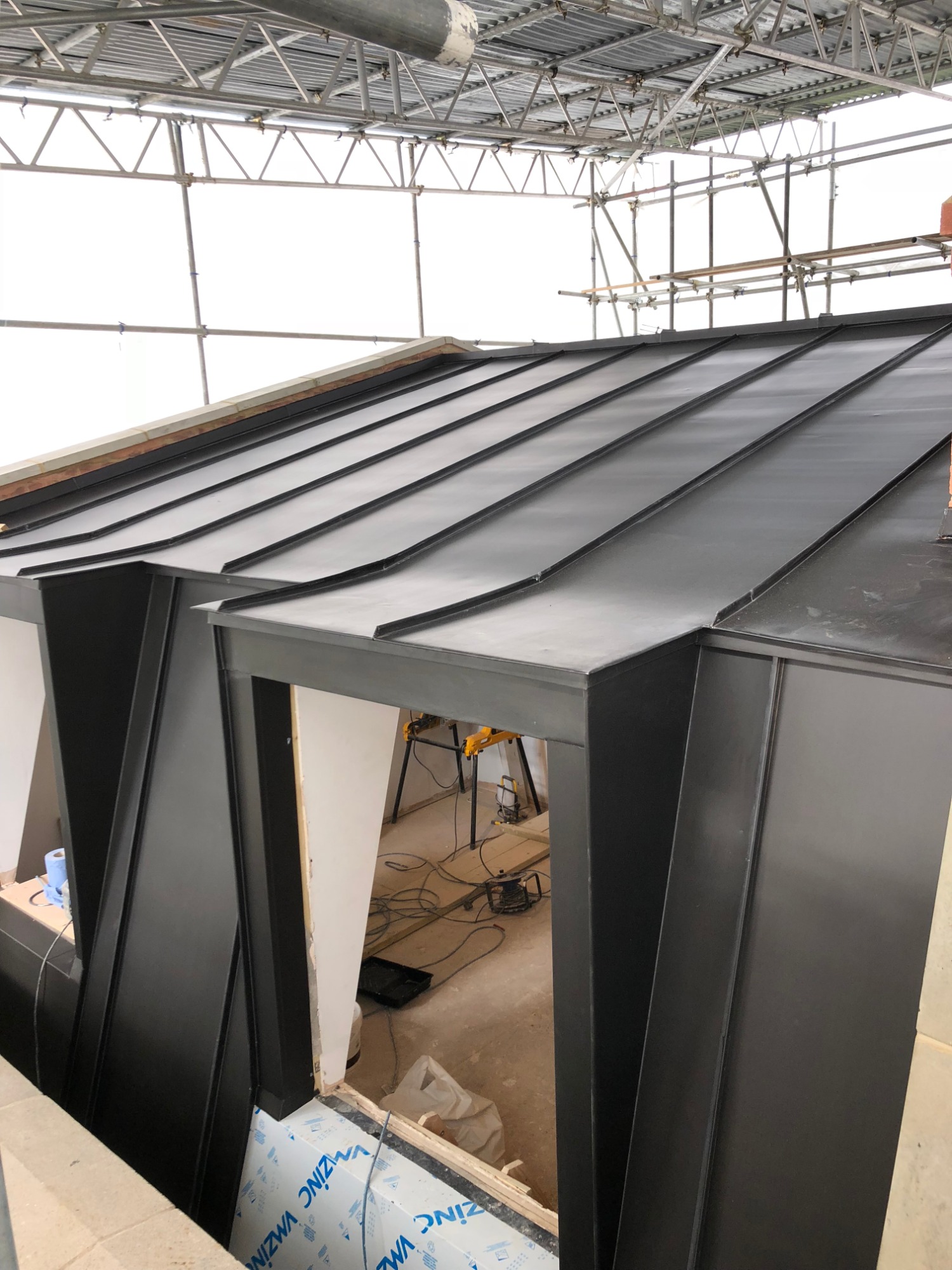 Nowoczesny, czarny dach z blachy na lukarnie, widok z góry, z rusztowaniem w tle, częściowo ukończony montaż.