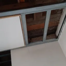 Montaż sufitu podwieszanego z widoczną konstrukcją metalową i częściowo zamontowaną białą płytą w Kole, z fragmentem ocieplenia widocznym w przestrzeni nad sufitem.