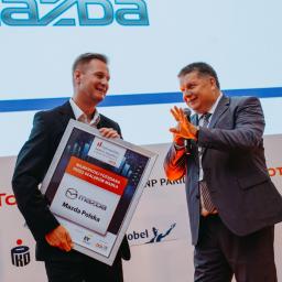 Zakład Pracy Kreatywnej - Dwóch mężczyzn w garniturach na scenie podczas wręczania nagrody dla Mazda Polska, na tle logo Mazda i sponsorów.