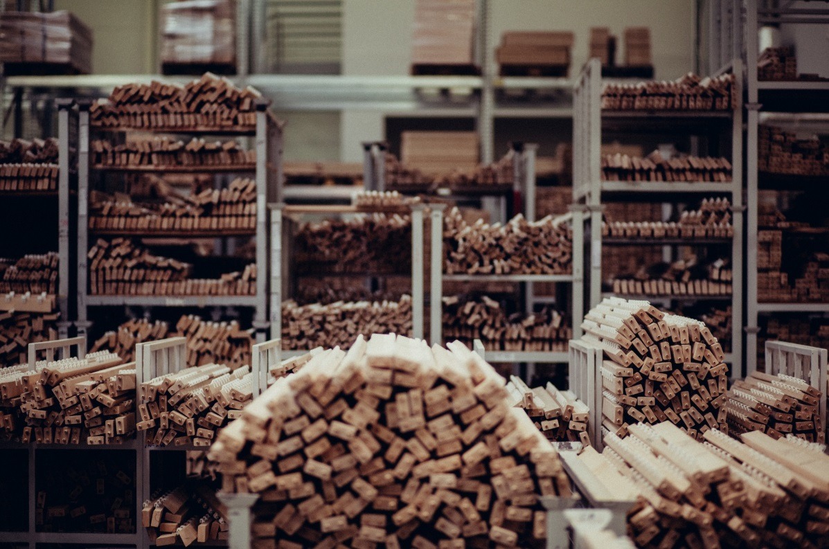 Magazyn z półkami pełnymi ułożonych elementów drewnianych, prawdopodobnie fragmentów mebli lub innych konstrukcji drewnianych, widoczne otwory i elementy mocujące.