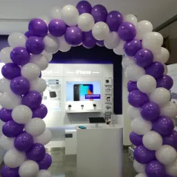 Arka z białych i fioletowych balonów przed wejściem do salonu telefonii komórkowej z napisem iPhone na ekranie.