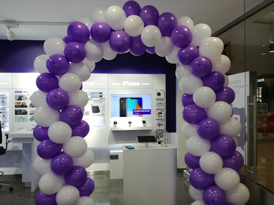 Arka z białych i fioletowych balonów przed wejściem do salonu telefonii komórkowej z napisem iPhone na ekranie.