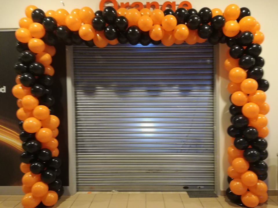 Brama rolowana ozdobiona girlandą z czarnych i pomarańczowych balonów, tworzących łuk.