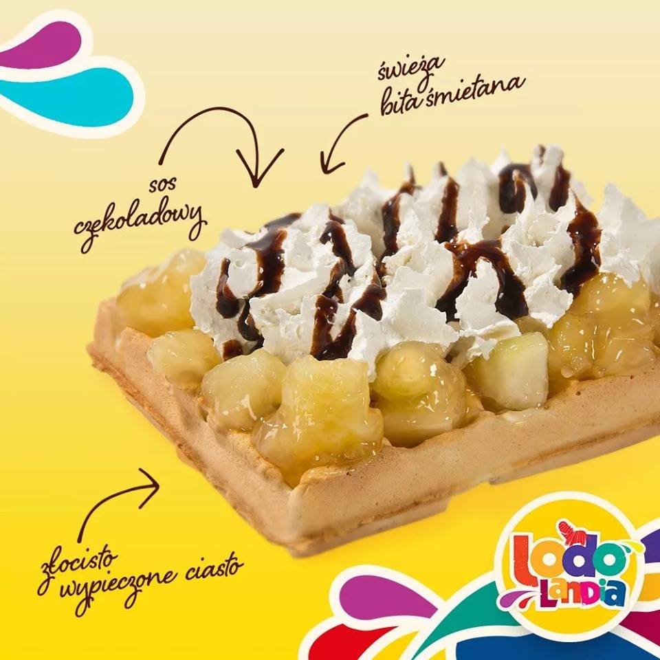 Kwadratowy gofr z kawałkami owoców w syropie, bitą śmietaną i polewą czekoladową, na żółtym tle z logo firmy.