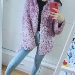 Kobieta robi selfie w lustrze, ubrana w fioletowe futerko, czarną bluzkę i jasne jeansy.