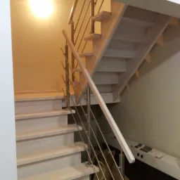 Jasne, drewniane schody z metalową balustradą w nowoczesnym wnętrzu, widok z dołu, butelka wody na dolnej półce schodów.