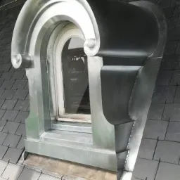 Okno lukarna z ozdobną, metalową obróbką blacharską na dachu pokrytym łupkiem.
