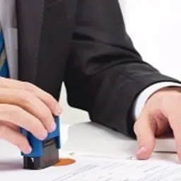 Mężczyzna w garniturze przykłada pieczęć do dokumentu, obok statuetka Temidy