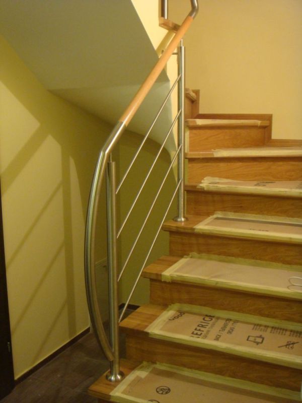 Nierdzewna balustrada z drewnianym poręczą na schodach z zabezpieczeniami kartonowymi na stopniach, żółta ściana w tle.