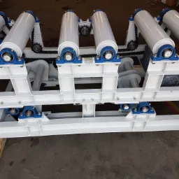 Fragment konstrukcji przenośnika rolkowego z napędem łańcuchowym, pomalowany na biało i szaro, widoczne łożyska w kolorze niebieskim, silnik elektryczny w dolnej części ramy.