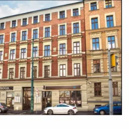 Fasada kamienicy z szyldem firmy, zaparkowane samochody, widok z ulicy.