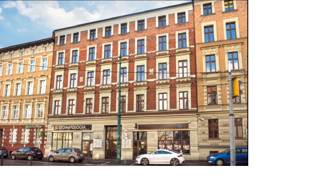 Fasada kamienicy z szyldem firmy, zaparkowane samochody, widok z ulicy.