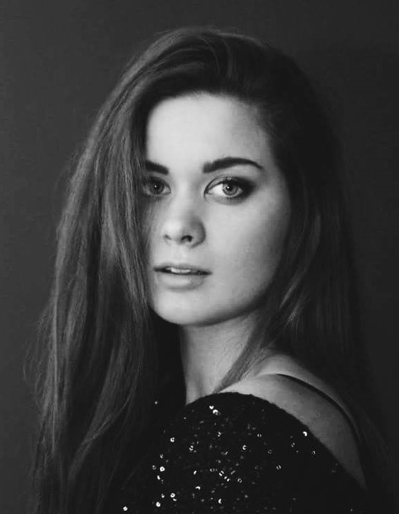 Portret młodej kobiety z długimi włosami, w czarno-białej tonacji, z delikatnym uśmiechem i błyszczącą sukienką.