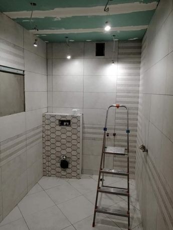 Remontowana łazienka z częściowo położonymi białymi płytkami, widoczne niedokończone podłączenia elektryczne i drabina aluminiowa.