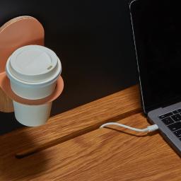 Wycinamy.to - Drewniany organizer na biurko z uchwytem na kubek z kawą i podłączonym do laptopa kablem zasilającym.