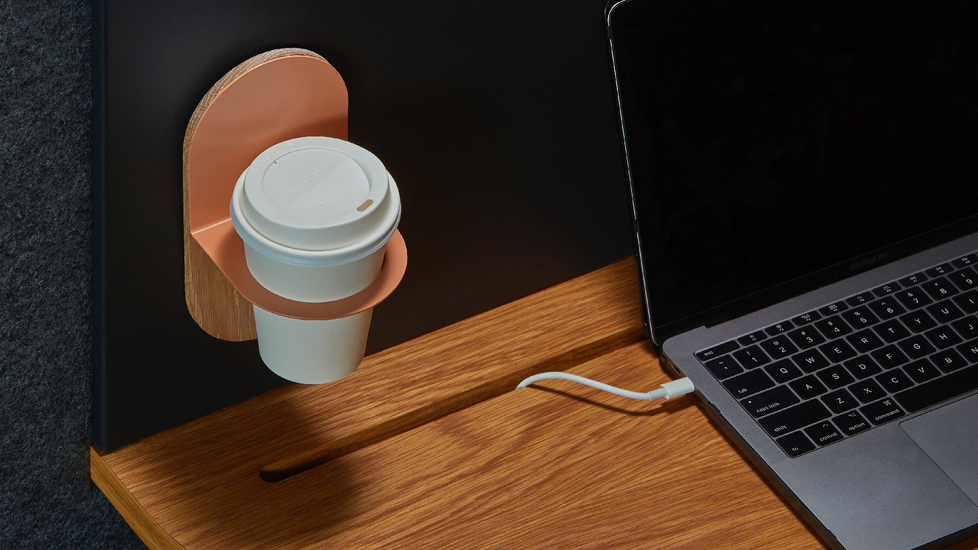 Drewniany organizer na biurko z uchwytem na kubek z kawą i podłączonym do laptopa kablem zasilającym.
