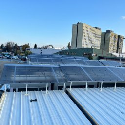 DKS Drewniane Konstrukcje Szkieletowe MARCIN BADOWSKI - Montaż zadaszenia z poliwęglanu na konstrukcji z blachy trapezowej, widoczne elementy mocujące i uszczelnienia, w tle zabudowania miejskie