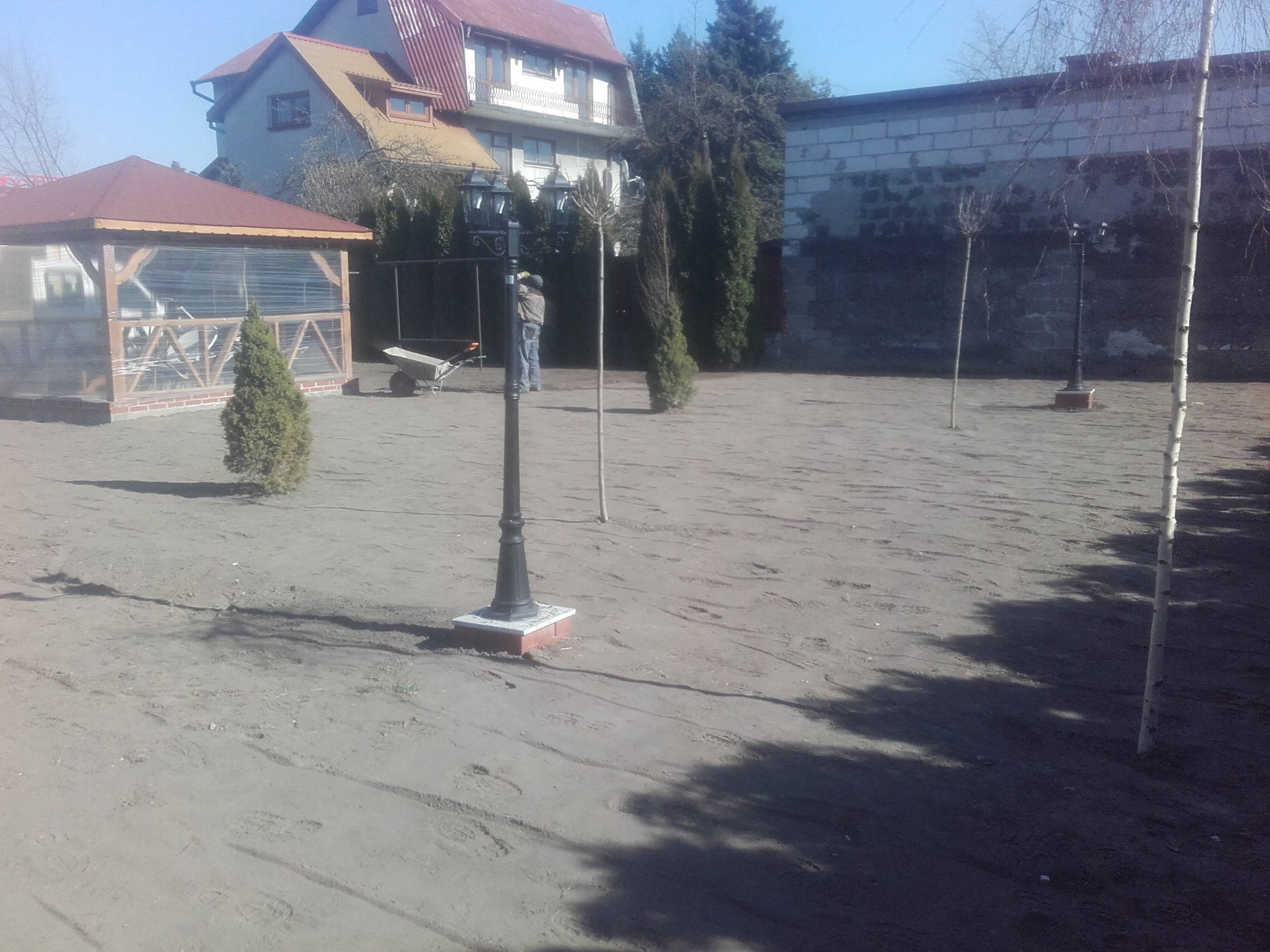 Przygotowanie terenu pod trawnik z siewu, widoczne ślady po grabieniu, lampa ogrodowa i młode drzewka.