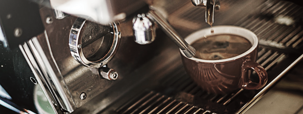 Detaliczny widok na profesjonalny ekspres do kawy podczas przygotowywania espresso do czerwonego kubka, z widoczną dyszą i kroplami kawy wpadającymi do napoju.