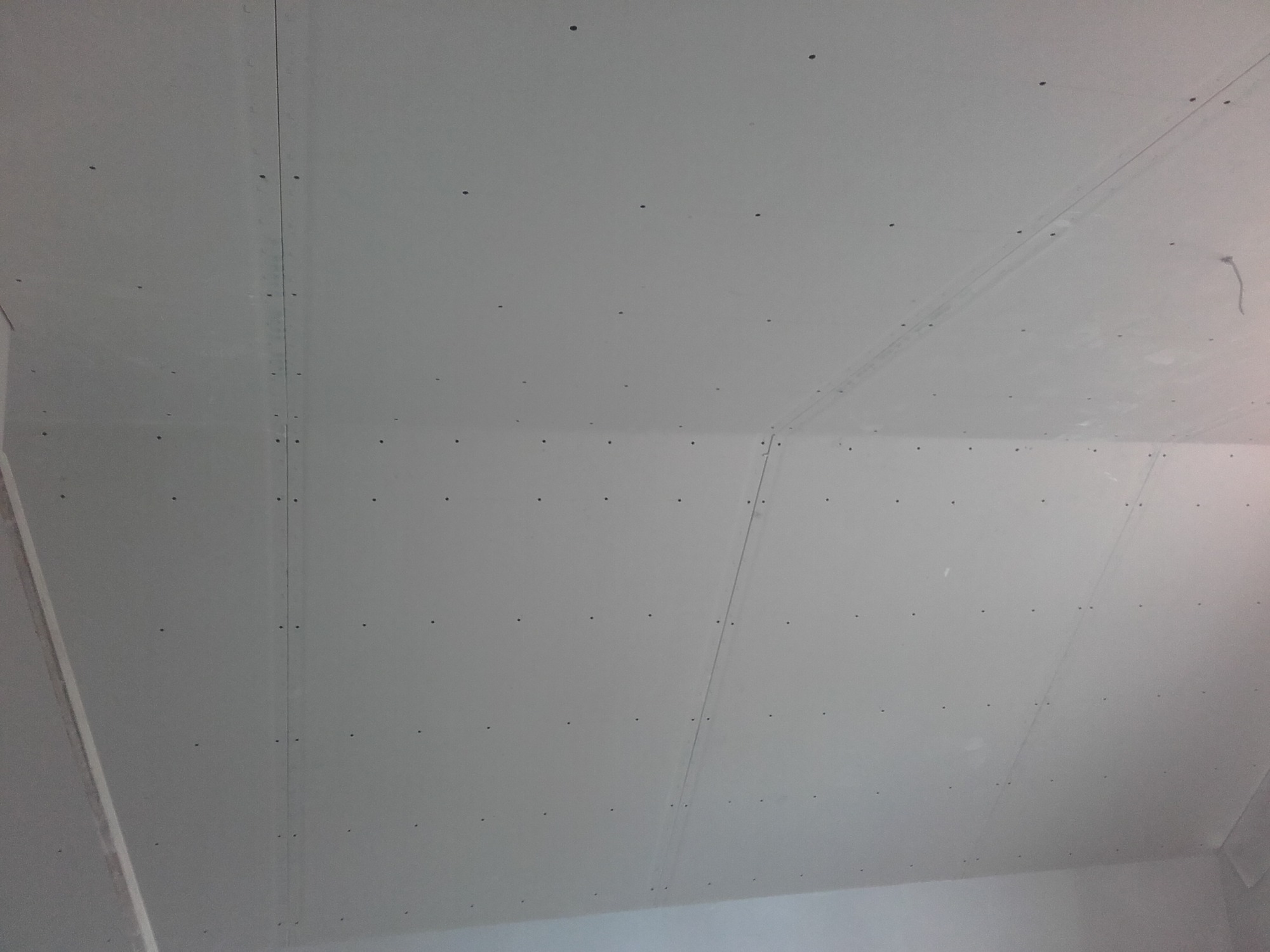 Wnętrze w trakcie montażu płyt gipsowo-kartonowych na suficie, widoczne śruby mocujące i łączenia płyt.
