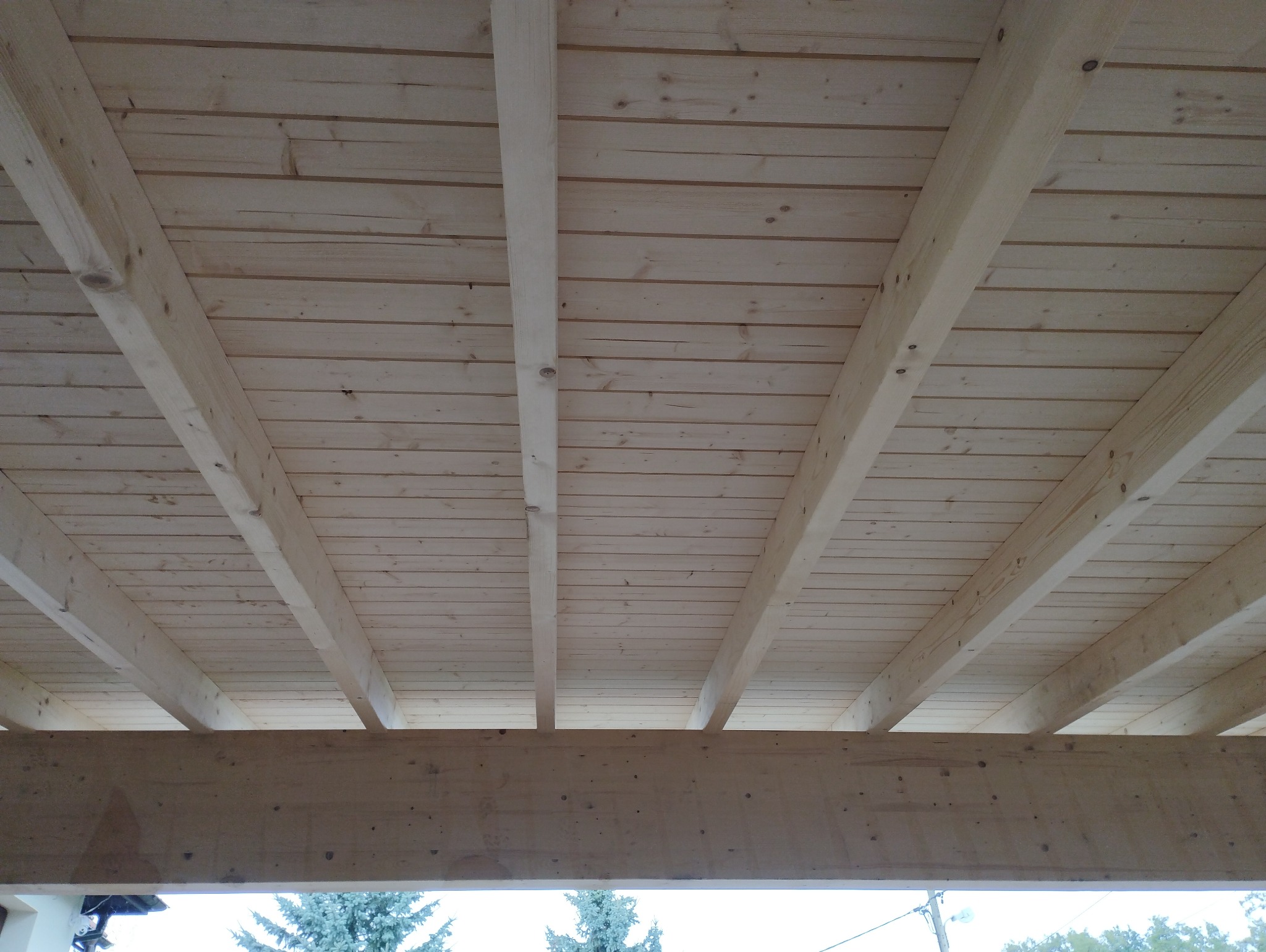 Surowy drewniany szkielet z belek i desek, widok z dołu, ukazujący konstrukcję z jasnego drewna przed dalszym wykończeniem.