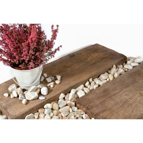 Dekoracyjna kompozycja z dwóch poziomych, brązowych płyt imitujących drewno, białych kamieni i wrzosu w białym wiaderku, na białym tle.