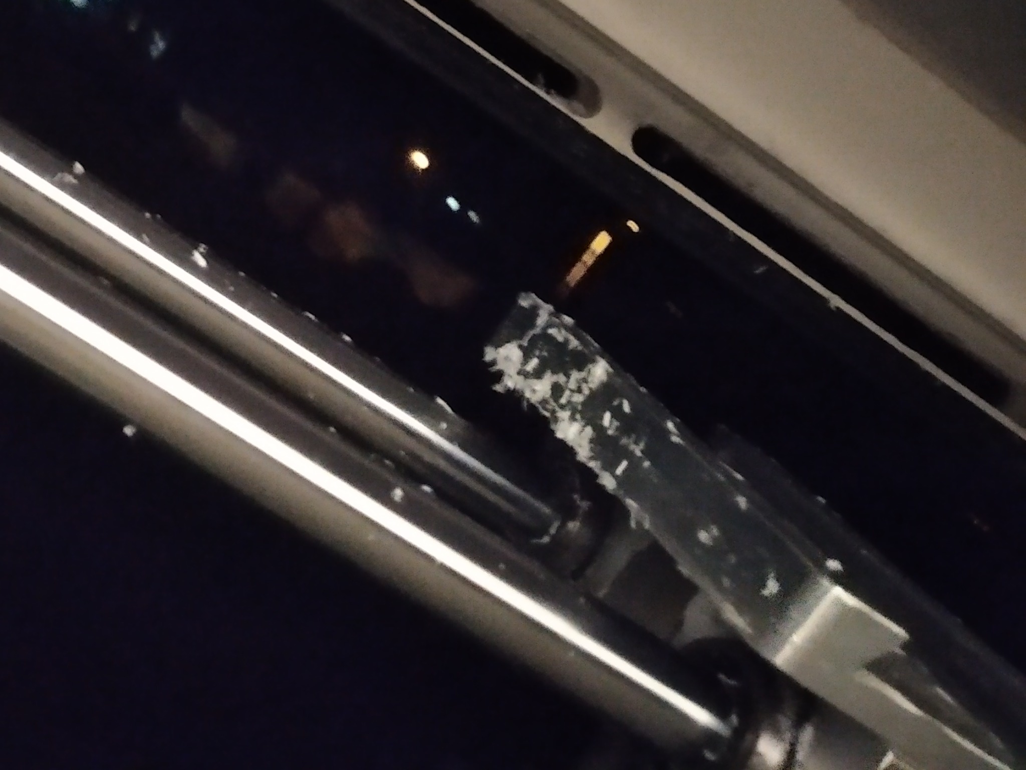 Uszczelka okienna pokryta białym osadem, widok z bliska, ciemne tło z odbiciami świateł.