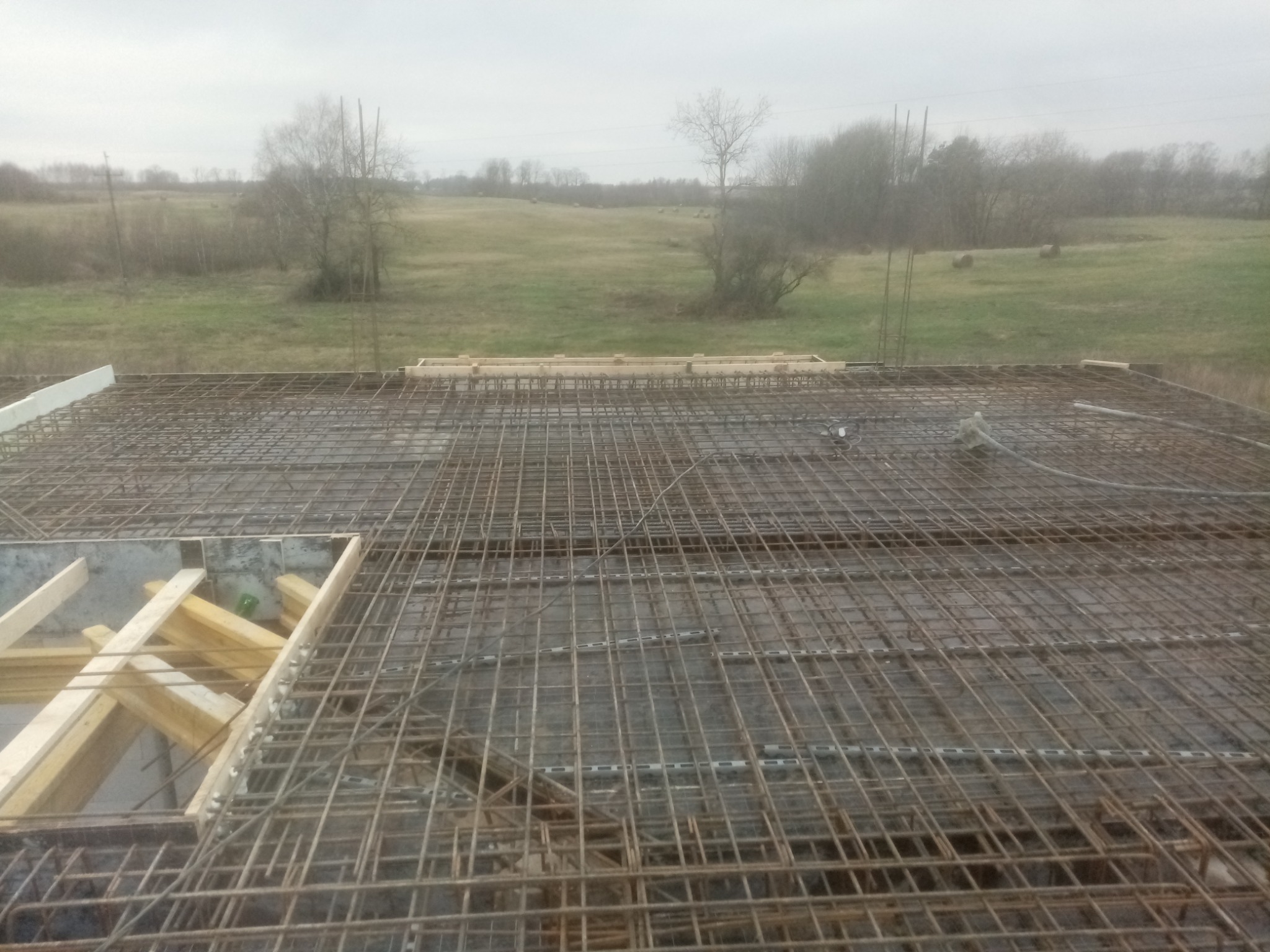 Siatka zbrojeniowa na przygotowanej konstrukcji, widok z góry na tle zalesionego krajobrazu w pochmurny dzień.