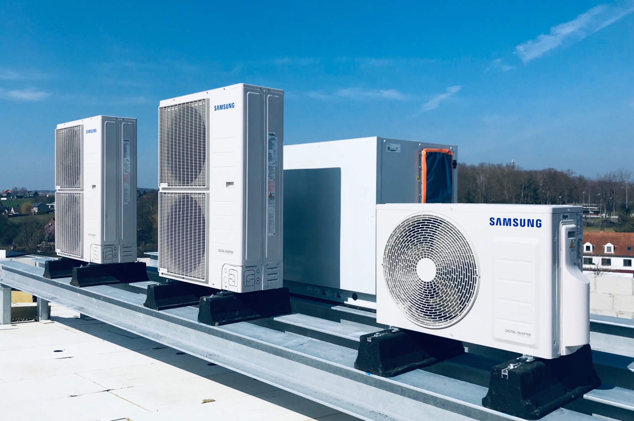 Cztery jednostki zewnętrzne klimatyzacji Samsung Digital Inverter na dachu płaskim, widok z boku, z widocznym krajobrazem w tle.