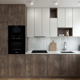 Zarosa Studio - Nowoczesna kuchnia z drewnianymi szafkami dolnymi i białymi górnymi, wyposażona w czarny piekarnik Bosch, płytę indukcyjną i marmurowy backsplash.