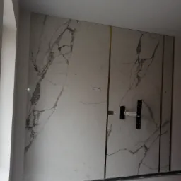 Ściana wyłożona płytami imitującymi marmur z złotymi paskami we Wrocławiu, z zamontowanym uchwytem do telewizora, w trakcie prac wykończeniowych.