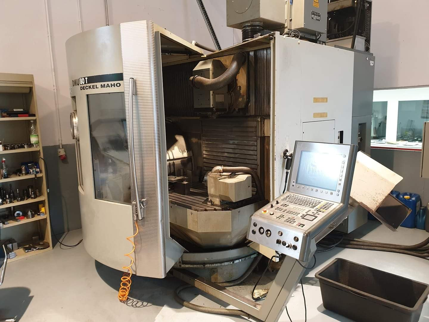 Pięcioosiowa frezarka pionowa Deckel Maho DMU 80 T z otwartymi drzwiami, widoczny surowiec wewnątrz komory roboczej i panel sterowania z ekranem.