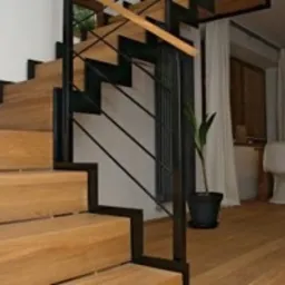 Nowoczesne schody drewniane z czarną, metalową konstrukcją i diagonalnymi prętami, prowadzące na górę w jasnym wnętrzu.