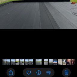 Hydroizolacje Makowski Konrad - Czarny, płaski dach pokryty papą termozgrzewalną, widok z góry. Widoczne łączenia papy i fragment obróbki blacharskiej. W tle zielona trawa.