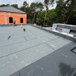 Hydroizolacje Makowski Konrad - Montaż papy termozgrzewalnej na płaskim dachu budynku w stanie surowym otwartym, widoczne narzędzia i materiały izolacyjne.