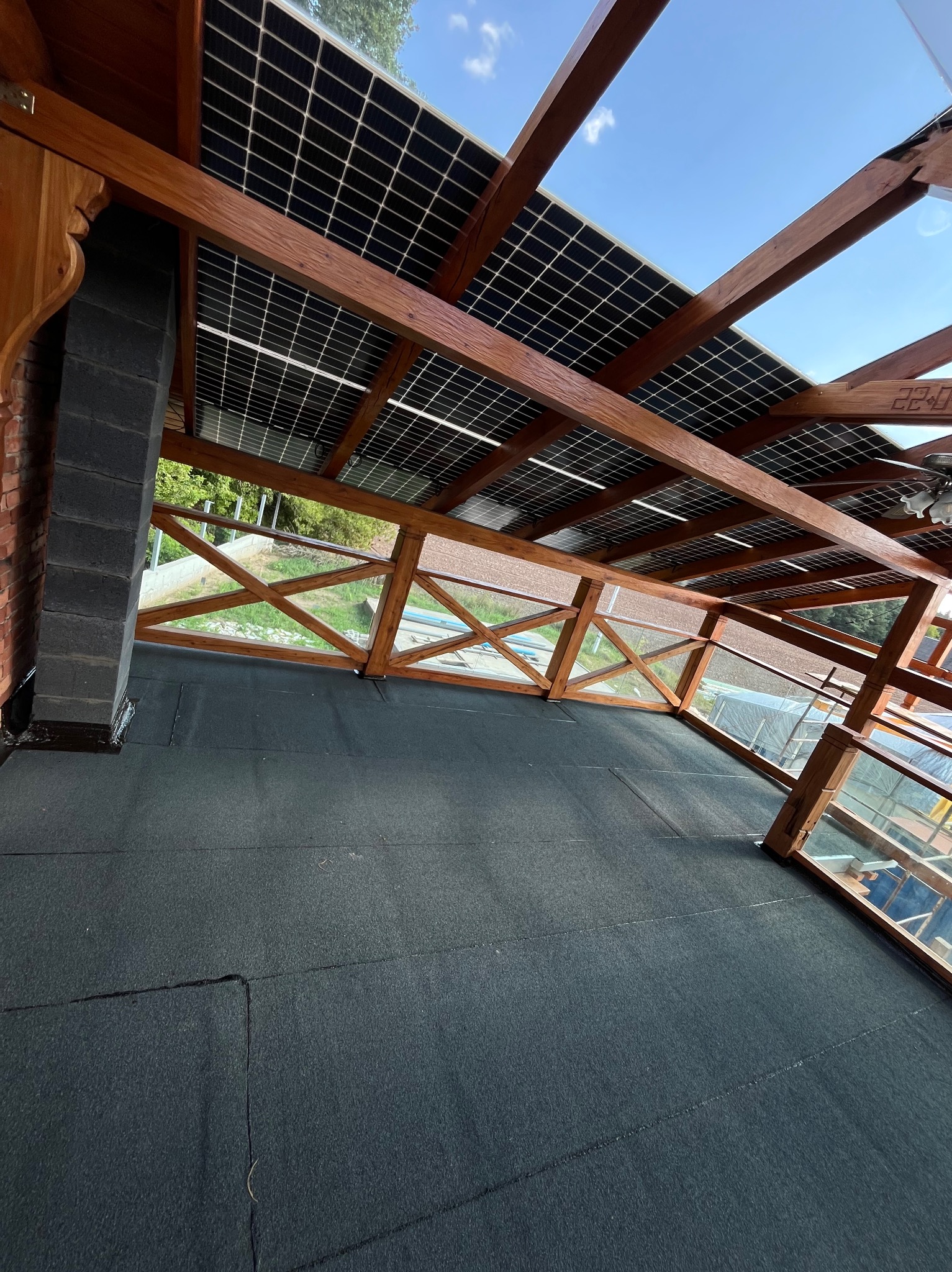 Wykończony dach z papy z drewnianą konstrukcją, panelami słonecznymi i kominem z cegły. Widok z góry na płaską powierzchnię dachu i elementy konstrukcyjne.