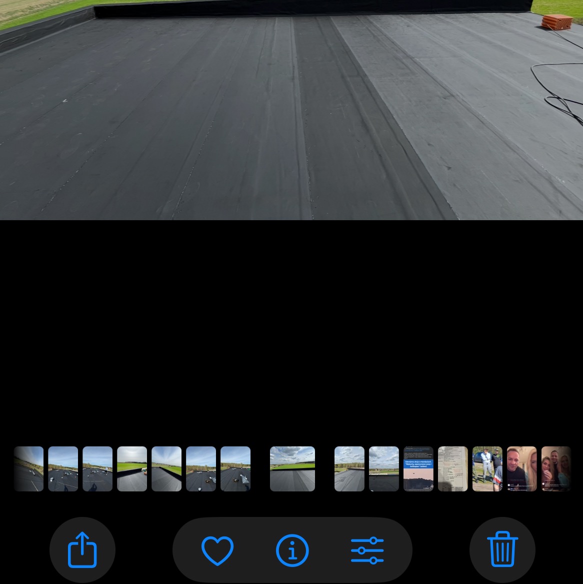 Czarny, płaski dach pokryty papą termozgrzewalną, widok z góry. Widoczne łączenia papy i fragment obróbki blacharskiej. W tle zielona trawa.