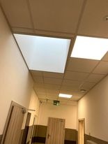 Korytarz biurowy z zamontowanym podwieszanym sufitem kasetonowym z oświetleniem LED, widoczne drzwi i system wentylacji pod sufitem.