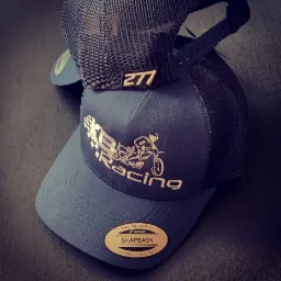 Dwie niebieskie czapki typu snapback z siateczkowym tyłem. Jedna z wyhaftowanym logo 'KR Racing' z motocyklistą, druga z małą naszywką z numerem '277'.