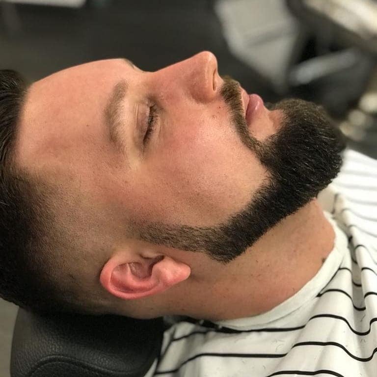 Mężczyzna z zamkniętymi oczami leży na fotelu z nowo wystylizowaną brodą i przyciętymi włosami.