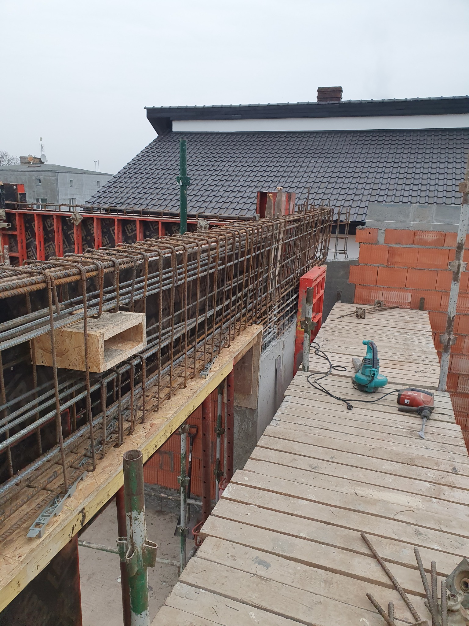Konstrukcja zbrojeniowa z deskowaniem na budowie, widoczne narzędzia i cegły w tle.